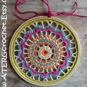 Puede incluir: Un mandala de ganchillo colorido con hilo rosa, verde, naranja y azul, enmarcado en un aro de madera. El mandala está colgado de un cordón rosa. El texto "pdf pattern" está escrito debajo del mandala.