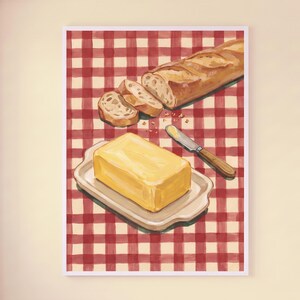 Könnte beinhalten: Ein vertikaler Wandkunstdruck mit einer Aquarellillustration eines goldenen, aufgeschnittenen Baguettes und einem Block gelber Butter auf einer weißen Keramikschale, begleitet von einem Buttermesser, vor einem rot-weiß karierten Hintergrund.