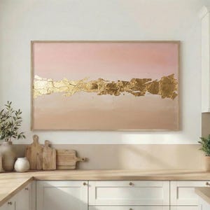 Könnte beinhalten: Gerahmtes abstraktes Gemälde mit rosa-beigem Hintergrund und strukturierten Goldblattdetails. Das Kunstwerk hängt über einer Küchenzeile mit Holzschneidebrettern und dekorativen Vasen.
