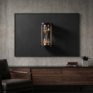 Könnte beinhalten: Eine Wand-Sanduhr mit einem schwarzen, kreisförmigen Rahmen mit metallisch goldenen Akzenten und klaren Glaskolben, die mit feinem goldenen Sand gefüllt sind, mittig auf einer großen, rechteckigen schwarzen Platte an einer Betonwand.