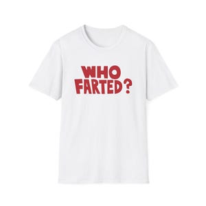 May include: A white short-sleeved t-shirt featuring the text WHO FARTED? printed in bold red capital letters across the center of the chest. The garment has a standard crew neckline and a straight hemline, made of a plain white fabric.