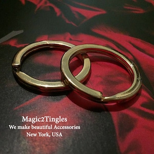 May include: Two gold-colored metal key rings, one slightly larger than the other, are lying on a red surface. The rings are interlocked, creating a decorative design.