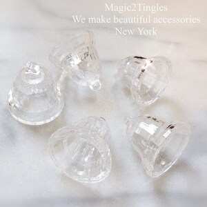 May include: Five clear glass bells with a faceted design. The bells are arranged in a circle on a white surface.