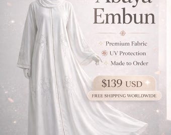 May include: A white Abaya Embun dress with long sleeves and a matching head covering. The dress features floral embroidery and a vertical line of embellishments down the front. The text "Abaya Embun" is displayed.
