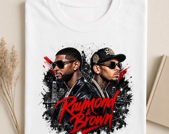Peut inclure: Un t-shirt blanc avec une impression graphique représentant deux hommes portant des lunettes de soleil et des vestes noires. Le motif inclut une silhouette de ville, des éclaboussures de peinture noire et le texte rouge "Raymond & Brown".