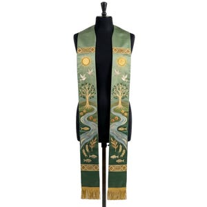 May include: A sage green liturgical stole featuring embroidered designs of a golden sun, white doves, a tree, a flowing blue river, and fish. The garment includes gold-toned decorative bands at the top and bottom, finished with gold fringe at the ends.