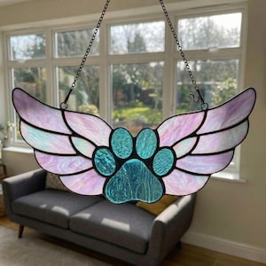 May include: Stained glass suncatcher featuring a paw print design in the center, flanked by iridescent wings. The wings are a blend of pink, purple, and blue hues. The suncatcher hangs from a chain, perfect for a window or wall decor.