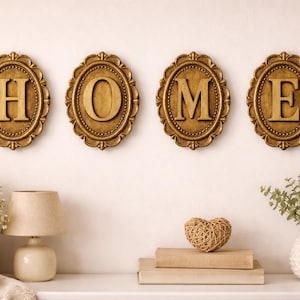 May include: Four oval wall plaques with gold-toned ornate frames, each featuring a single raised letter spelling the word HOME. The letters H, O, M, and E are centered within the frames, which have a textured, beaded edge design.