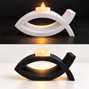 May include: Two fish-shaped candle holders, one white and one black, each featuring a smooth, curved frame with a circular cutout at the top. A small, round, cream-coloured tea light candle with a glowing yellow flame sits inside each holder.