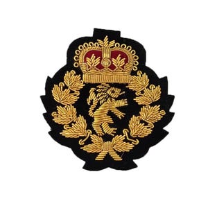 May include: A black embroidered patch featuring a gold crown and a lion rampant. The crown is atop a red background, and the lion is surrounded by gold leaves. The patch has a black border.