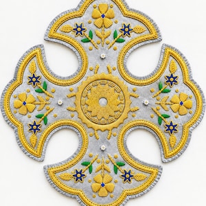 Puede incluir: Un tapiz de pared en forma de cruz hecho de fieltro gris, con intrincados bordados de cordón amarillo, motivos florales azules y amarillos, y detalles de hojas verdes. El centro muestra un patrón circular amarillo con pequeñas flores blancas.