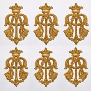 May include: Six identical gold-colored embroidered patches arranged in two rows of three. Each patch features a symmetrical, ornate crest design topped with a crown, characterized by intricate swirling lines and pointed floral-like motifs.