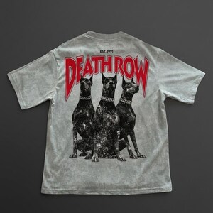May include: Light grey t-shirt with a graphic of three black dogs wearing silver chain collars. The red text "DEATH ROW" is above the dogs, with "EST. 1991" above the text. The shirt has a vintage, distressed appearance.
