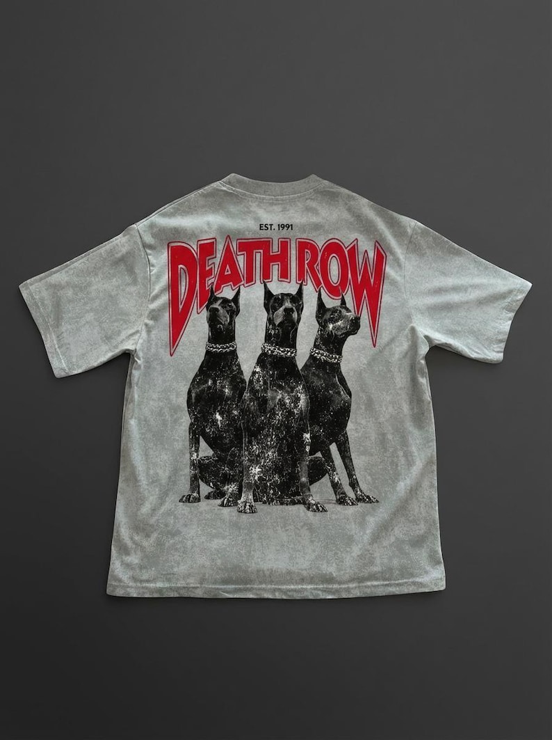 May include: Light grey t-shirt with a graphic of three black dogs wearing silver chain collars. The red text "DEATH ROW" is above the dogs, with "EST. 1991" above the text. The shirt has a vintage, distressed appearance.