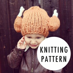May include: A child wearing a knitted orange and white turkey hat. The hat has two large, round, white pom-poms on the top. The child is wearing a brown leather jacket. The text "KNITTING PATTERN" is written in black on a white circle.