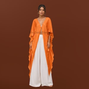 May include: A bright orange open-front kaftan with wide, flowing sleeves and a deep V-neckline, paired with floor-length white wide-leg trousers. The text "SheOwnsTheLook" is printed in the center of the orange garment.