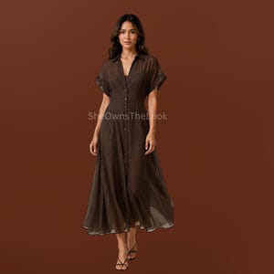 May include: A dark brown midi-length shirt dress featuring short sleeves, a classic collar, and a full-length button-down front. The garment is made of a sheer, lightweight fabric and includes the text SheOwnsTheLook printed on the front.