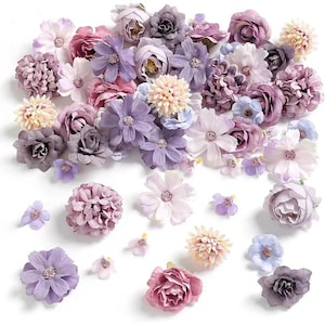 May include: A collection of artificial flowers in various shades of purple, pink, and cream. The assortment includes roses, daisies, and other floral designs, perfect for crafting or decorative purposes. The flowers are arranged on a white surface.