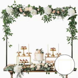 May include: A wedding or event display featuring a black metal arch adorned with white and blush-colored flowers and greenery. The table is set with a cake, cupcakes, and other desserts on gold stands, creating an elegant and festive atmosphere.