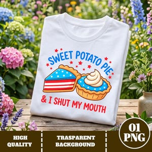 May include: White t-shirt with a graphic of two sweet potato pies, one slice and one whole, with blue and red accents. Text reads "SWEET POTATO PIE" and "& I SHUT MY MOUTH" in red. The shirt is displayed on a wooden surface.