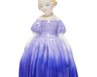 May include: A porcelain figurine of a person with light brown hair, wearing an off-the-shoulder dress that transitions from a light lavender color at the bodice to a deep, vibrant royal blue at the hem, featuring puffed sleeves and a full skirt.