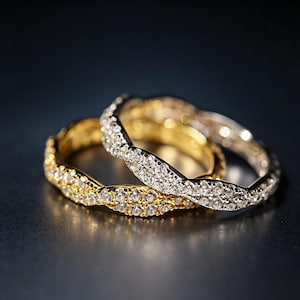 May include: Two intertwined rings, one gold and one silver, both encrusted with small, sparkling gemstones. The gold ring has a warm, radiant hue, while the silver ring has a cool, bright appearance. The rings are set against a dark background.