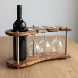 May include: A dark wood wine bottle and glass holder featuring a circular cutout for one bottle and three slots for hanging stemmed glasses. The structure is supported by four vertical silver metal rods with visible hardware nuts at the top.