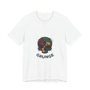 Può includere: T-shirt bianca con un design a teschio colorato e la scritta "GRUNGE" in nero. Il teschio è un mix di giallo, verde, rosso e blu. Il design ha un effetto invecchiato e macchiato.