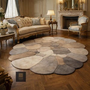Könnte beinhalten: Ein großer, runder Teppich mit einem Kieseldesign in Beige-, Grau- und Brauntönen. Der Teppich liegt auf einem Parkettboden in einem Wohnzimmer. Das Design des Teppichs ähnelt einer Ansammlung glatter Steine.