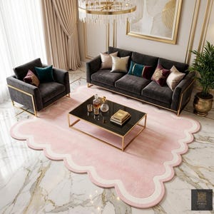 May include: A luxurious living room set featuring a dark gray sofa and armchair with gold trim, complemented by decorative pillows. A black glass coffee table sits on a pink, cloud-shaped rug. A chandelier hangs above.