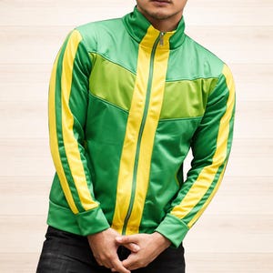 Könnte beinhalten: Grün-gelbe Trainingsjacke mit durchgehendem Reißverschluss. Die Jacke hat einen hohen Kragen und gelbe Streifen an den Ärmeln und Seiten. Die Jacke ist aus glänzendem Material gefertigt.