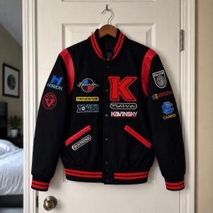 May include: A black varsity jacket with red leather sleeves and red striped ribbed trim at the collar, cuffs, and hem. The jacket features multiple embroidered patches including the text KAVINSKY, ZOMBIE, RENEGADE, HORIZON, PULSAR, CAMEO, and OUTSIDER.