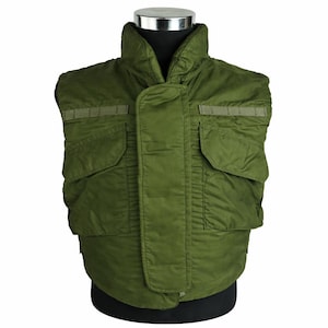 May include: An olive green military-style vest with a high collar and multiple pockets. The vest is displayed on a black mannequin, highlighting its quilted design and practical features. The vest has two rectangular pockets on the front.
