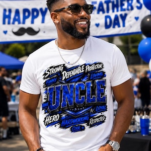 May include: A white short-sleeved t-shirt featuring a blue and black graphic design with the word UNCLE in large letters. Surrounding text includes the words STRONG, DEPENDABLE, PROTECTOR, LOVING, FUNNY, BRAVE, LOYAL, HERO, HARDWORKING, RESPECTED, and COOL.