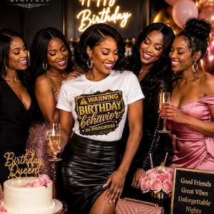 May include: A white t-shirt featuring a rectangular graphic with a yellow warning triangle and the text WARNING BIRTHDAY behavior IN PROGRESS in gold and black lettering. The design is centered on the chest of the shirt, which is worn with a black skirt.