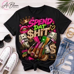 May include: A black t-shirt featuring a vibrant graphic print with the text "SPEND DAT SHIT" in gold and pink. The design includes stacks of hundred-dollar bills, various credit cards, a gold crown, pink lips, and a hand with long decorated nails.