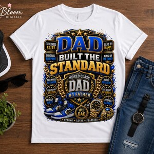 Peut inclure: Un t-shirt blanc avec un grand motif graphique complexe en bleu, or et noir. Le texte indique DAD BUILT THE STANDARD, WORLD CLASS DAD, #1 FATHER, et comprend des illustrations de baskets bleu et blanc, d'une montre en or et d'une bague en or.