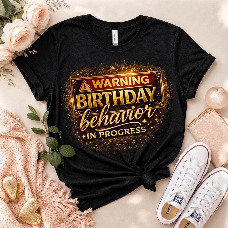 May include: A black short-sleeved t-shirt featuring a graphic print with a gold-bordered rectangular sign. The text reads WARNING BIRTHDAY behavior IN PROGRESS in gold and white lettering, surrounded by a sparkling gold glitter effect.