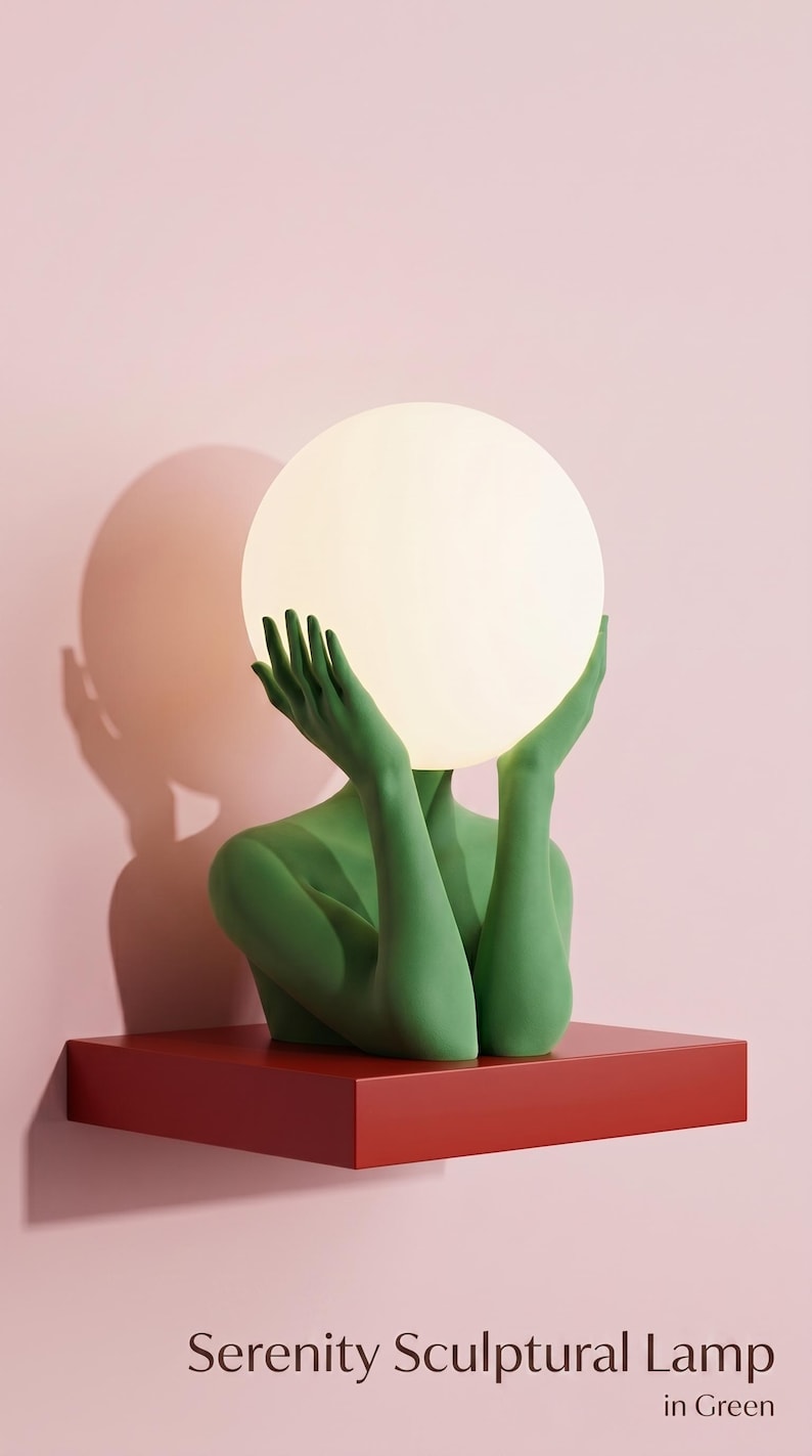 May include: A sculptural lamp featuring a green figure with raised arms holding a glowing white spherical light bulb. The figure is positioned on a flat red rectangular base. The text Serenity Sculptural Lamp in Green is printed below.
