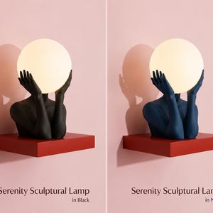 Puede incluir: Dos l&aacute;mparas esculturales Serenity, una en negro y otra en azul marino, que representan un torso humano con las manos levantadas sosteniendo una gran bombilla esf&eacute;rica blanca brillante. Las l&aacute;mparas est&aacute;n sobre estantes rojos.