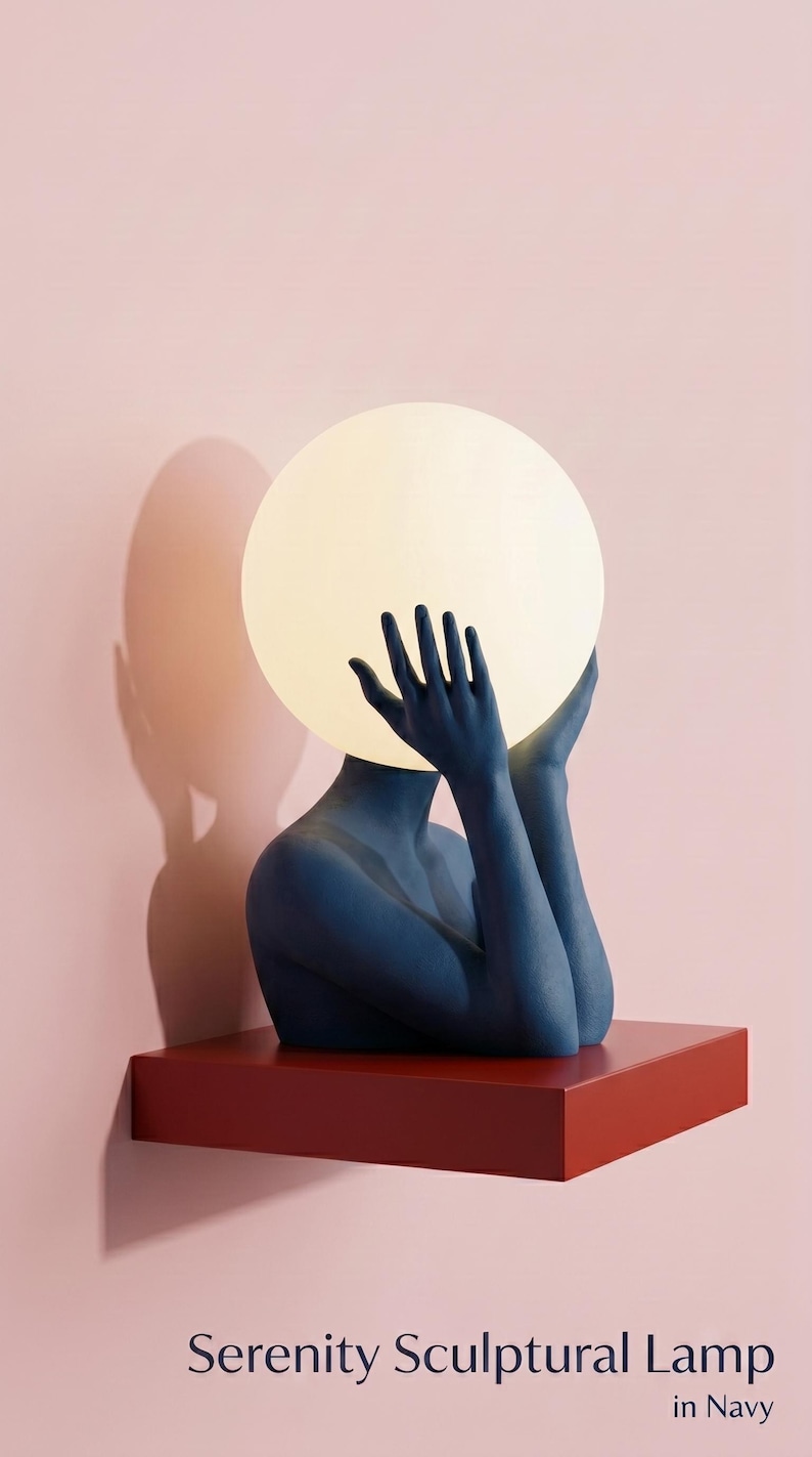 May include: A navy blue sculptural lamp featuring a figure with raised hands holding a glowing white spherical light bulb. The lamp rests on a rectangular red base. The text Serenity Sculptural Lamp in Navy is printed at the bottom of the image.