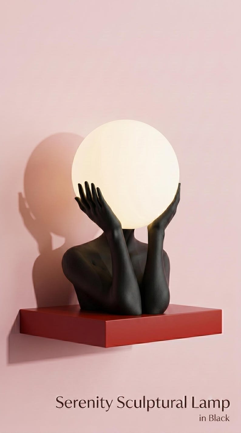 May include: A sculptural lamp featuring a matte black figure with arms raised, holding a large, glowing, spherical white glass shade. The base is a solid red rectangular shelf. The text Serenity Sculptural Lamp in Black is printed below.