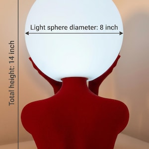 May include: A red lamp base shaped like a human torso supporting a white spherical light. The text on the image indicates a light sphere diameter of 8 inches and a total height of 14 inches. The lamp features a matte red finish and a smooth texture.