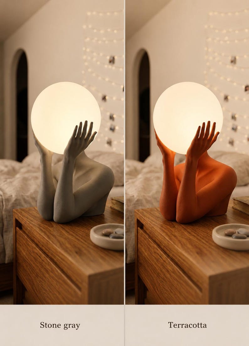 Puede incluir: Una l&aacute;mpara de mesa con una figura esculpida cuyos brazos levantados sostienen una bombilla esf&eacute;rica blanca brillante. La base est&aacute; disponible en dos acabados mate: un gris piedra neutro y un color terracota c&aacute;lido.