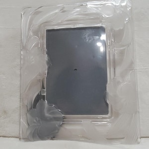May include: A rectangular picture frame made of clear glass with a frosted finish. The frame features embossed floral and leaf patterns along the borders, surrounding a central dark gray rectangular insert for a photograph.