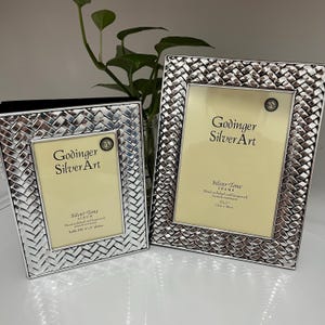 May include: Two silver-tone picture frames with a woven design border. The frames have a light yellow interior and the text "Godinger Silver Art". The smaller frame is for a 4" x 6" photo, and the larger frame is for a 5" x 7" photo.