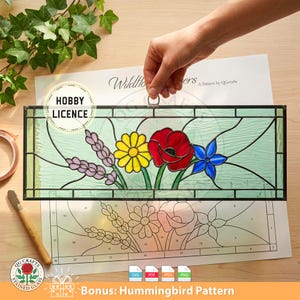 May include: Stained glass panel featuring a floral design with a red poppy, yellow daisy, blue flower, and purple lavender. The panel is held by a hand, with a pattern sheet below. The panel has a Hobby License.