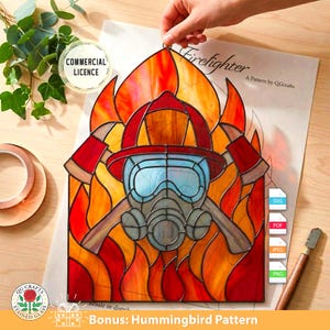 Può includere: Pannello in vetro colorato raffigurante un elmetto e un'ascia da pompiere su uno sfondo di fiamme. Il disegno include una maschera antigas e la parola "Firefighter". Il pannello è un modello di QG Crafts, con licenza commerciale.