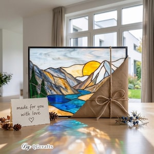 Peut inclure: Vitrail repr&eacute;sentant un paysage de montagne avec une rivi&egrave;re et un soleil couchant. L'&oelig;uvre est encadr&eacute;e en noir et envelopp&eacute;e dans du papier brun nou&eacute; avec de la ficelle. Une petite carte indique "made for you with love".