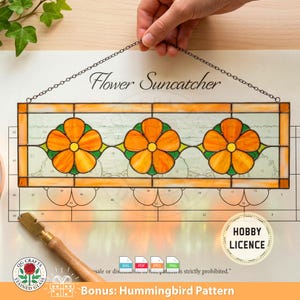 May include: A rectangular stained glass flower suncatcher with three orange flower designs. The suncatcher is suspended by a chain and features the text "Flower Suncatcher". Includes a "Hobby Licence" badge and a "Bonus: Hummingbird Pattern" offer.
